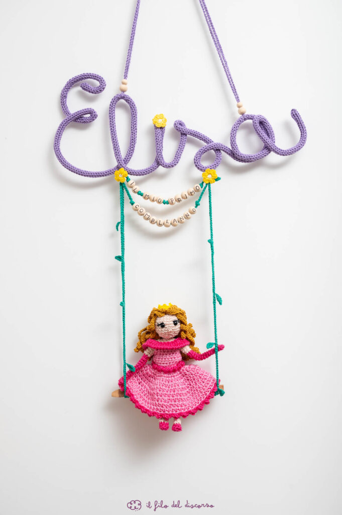 Creazione realizzata interamente a mano, all'uncinetto, per il primo compleanno di Elisa. Una principessa, realizzata in amigurumi, seduta su un'altalena appesa al suo nome, ed alla scritta in legno "il mio primo compleanno".